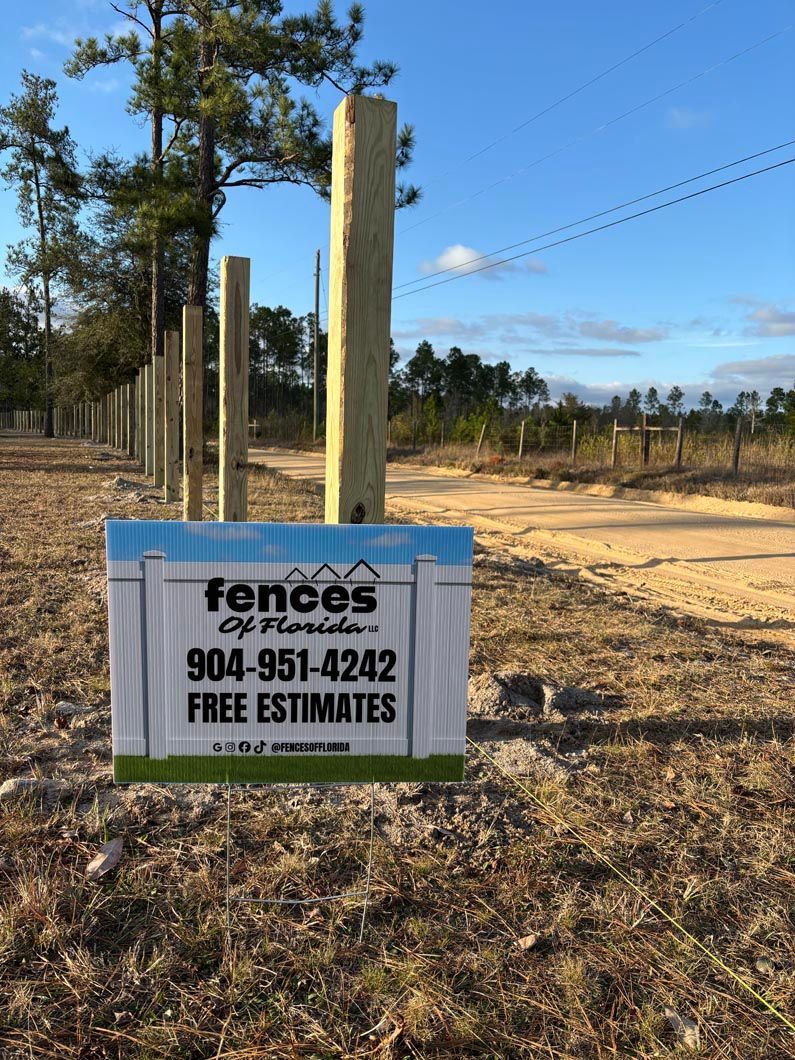 Fence posts lined along a dirt roadside with a sign advertising fence services and free estimates.