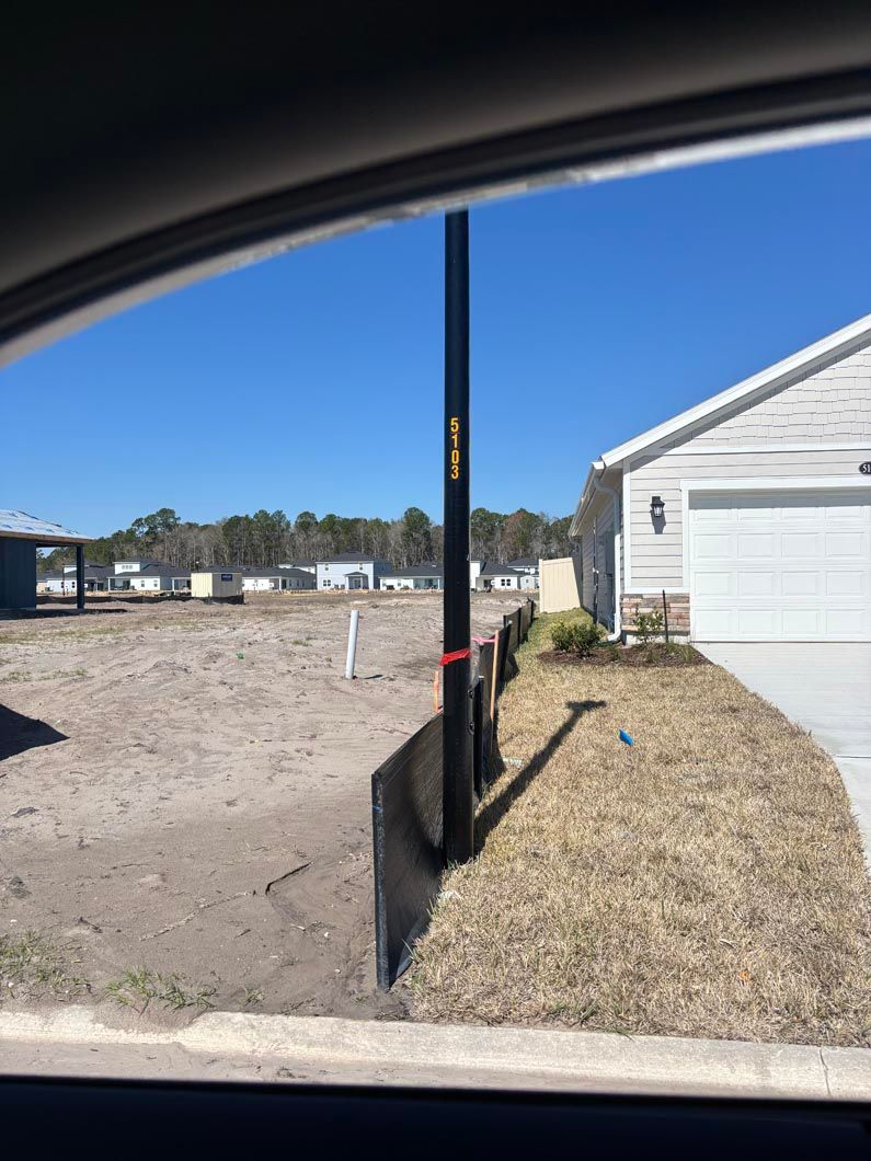 Yard with a utility pole beside a white house, showing a dirt lot and dry grass under a blue sky