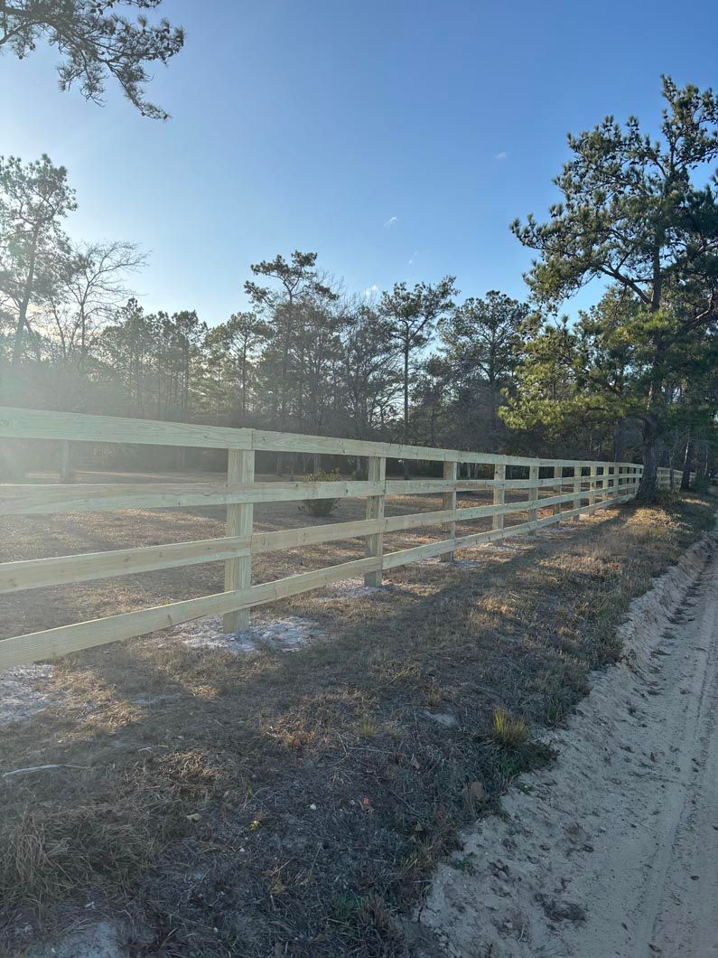 White wooden fence along a sandy road in a sunny wooded area