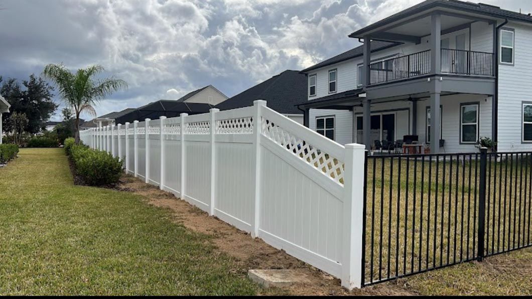 White fence and black gate beside a modern suburban house under a cloudy sky