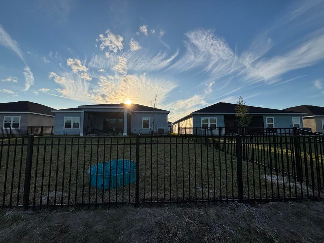 Suburban homes behind a black fence at sunset, with wispy clouds in a blue sky.