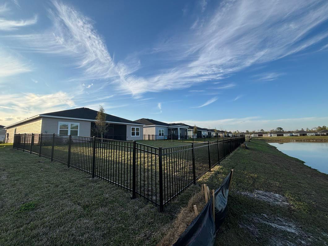 Black metal fence beside a pond, with houses and a blue sky at sunset