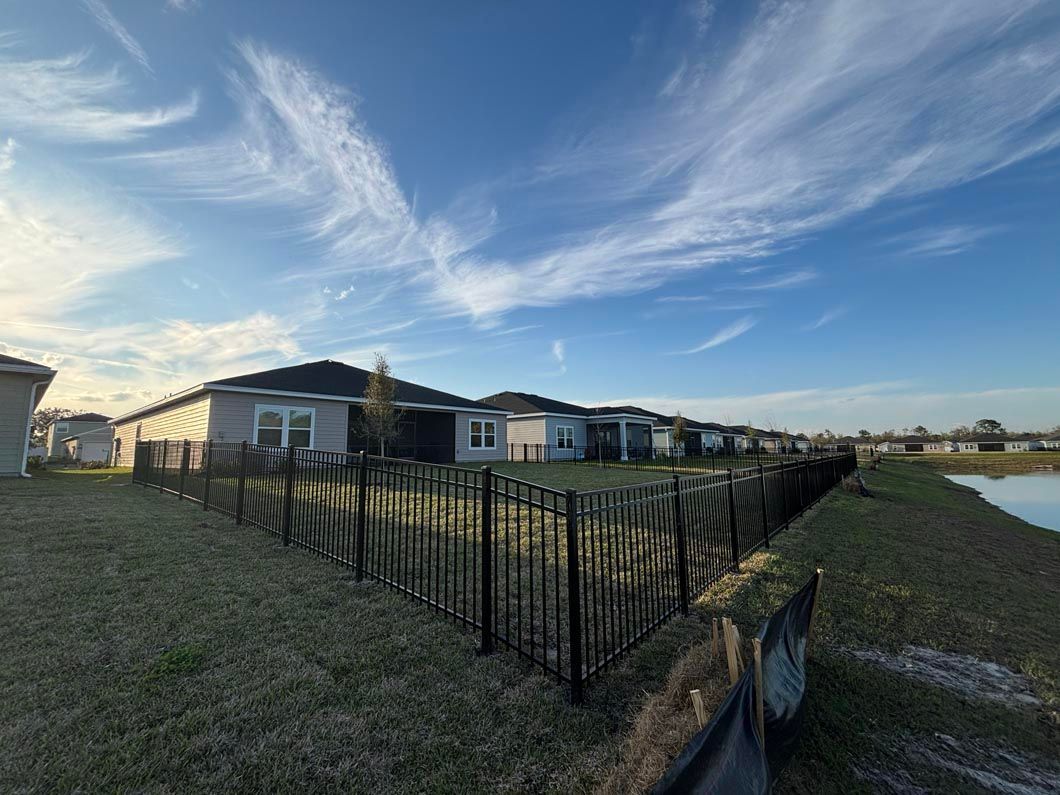 Row of modern houses beside a black metal fence under a bright blue, cloud-streaked sky