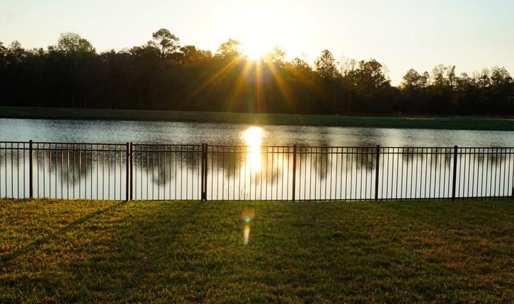 Sunrise over a calm lake with a wooden fence and trees silhouetted along the shore.