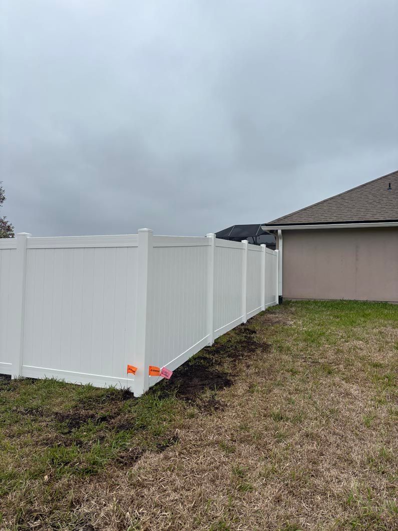 White vinyl fence along a yard beside a beige house under a cloudy sky