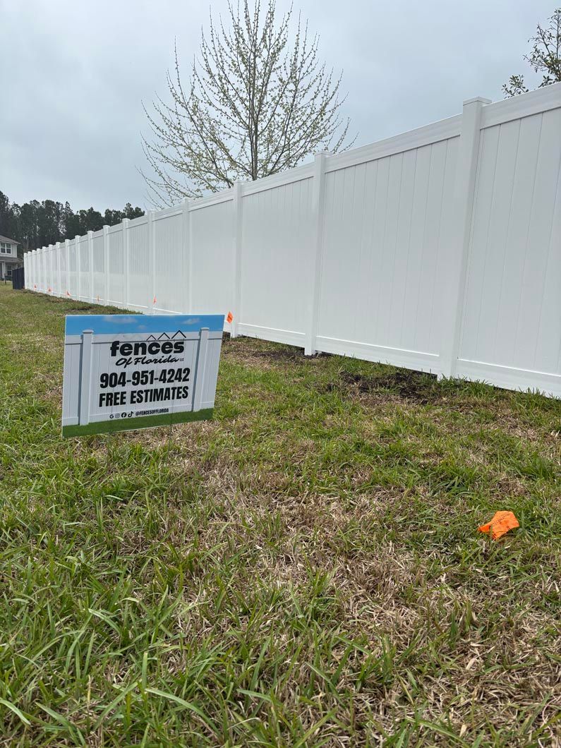 Fenced grassy lot with white privacy fence and a surveyor’s sign in the foreground.