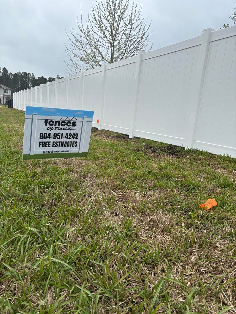 White fence with a sign in a grassy yard beside a tree and small orange marker