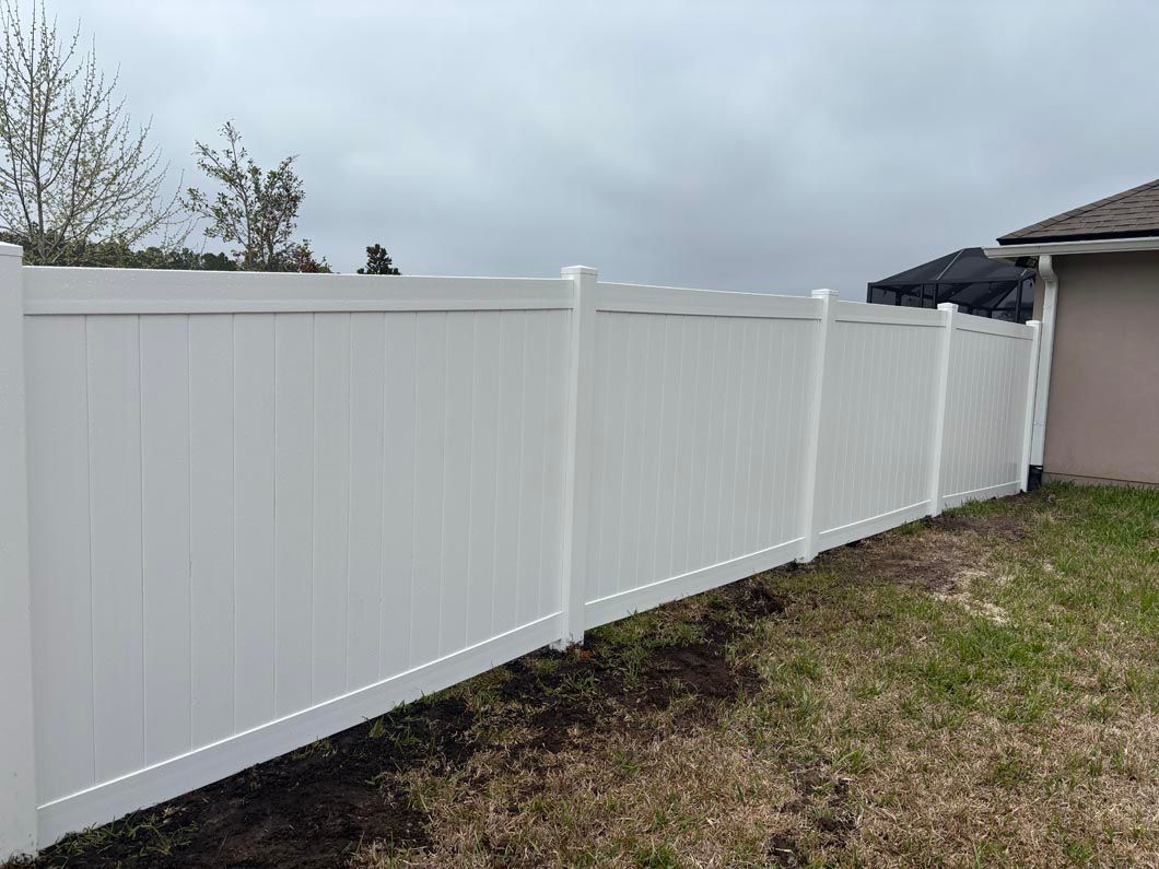 White vinyl fence along a grassy backyard beside a house under a cloudy sky