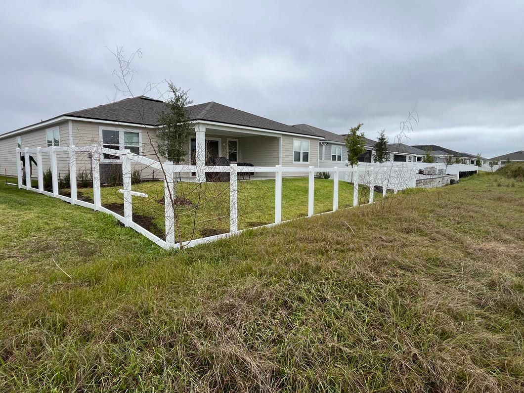 Suburban house with white fence and grassy yard under a cloudy sky