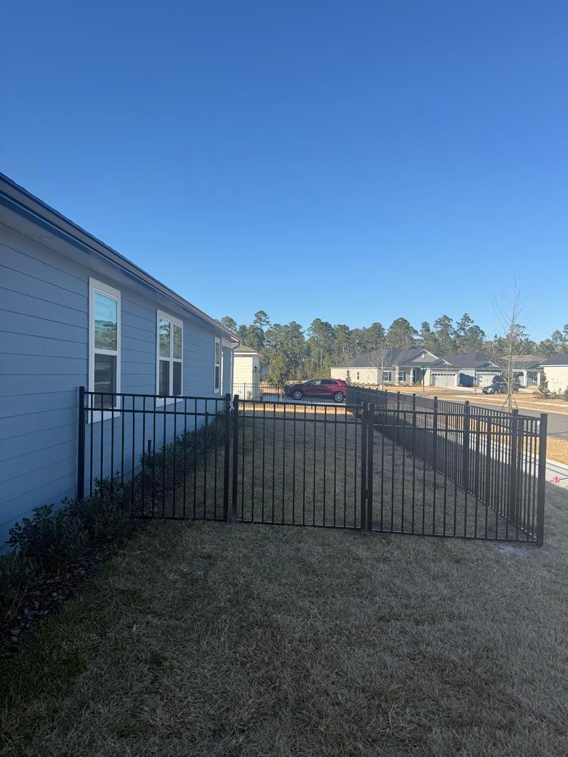Backyard with a black metal fence beside a white house under a clear blue sky
