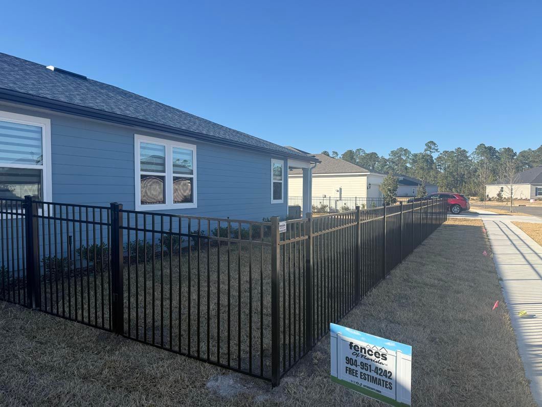 Blue house with black metal fence and gravel driveway under a clear sky