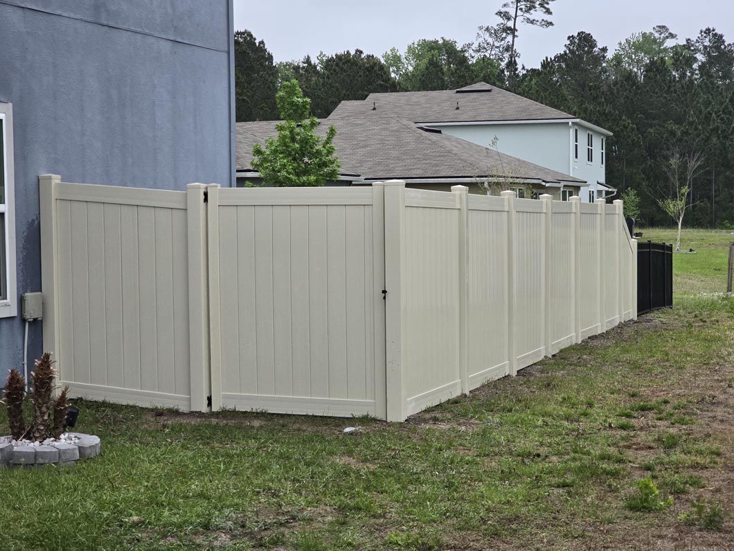 Beige privacy fence along a grassy yard beside a gray house and driveway.