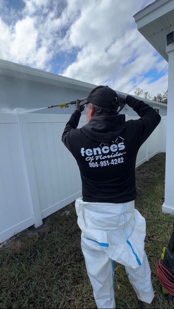 Person in black sweatshirt and white pants using a tool by a white fence outdoors.