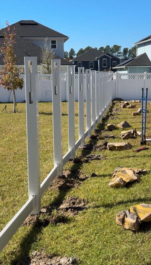 White fence posts and panels installed along a grassy yard beside houses on a sunny day