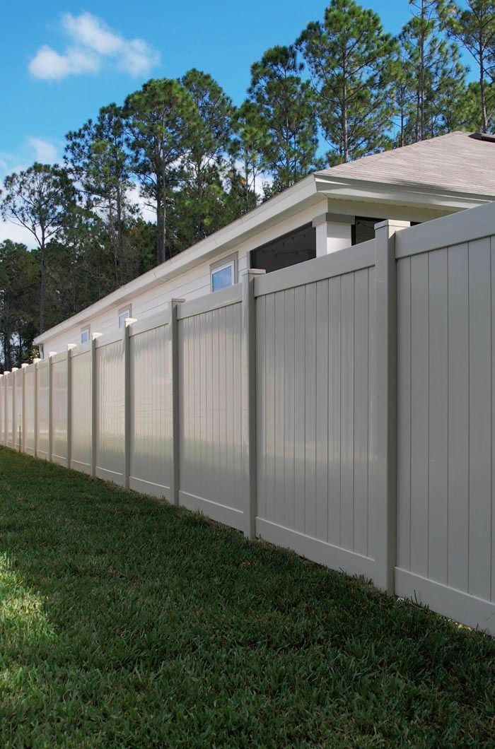 Tall light-gray vinyl fence beside a house with trees in the background