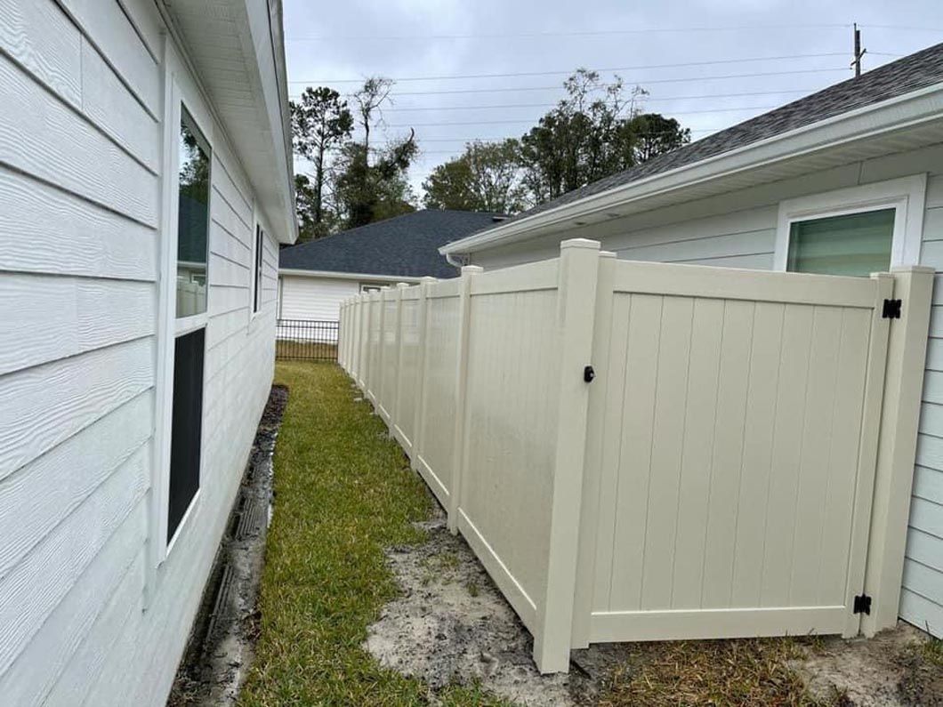 Narrow side yard with a beige vinyl fence beside a white house and gravel walkway