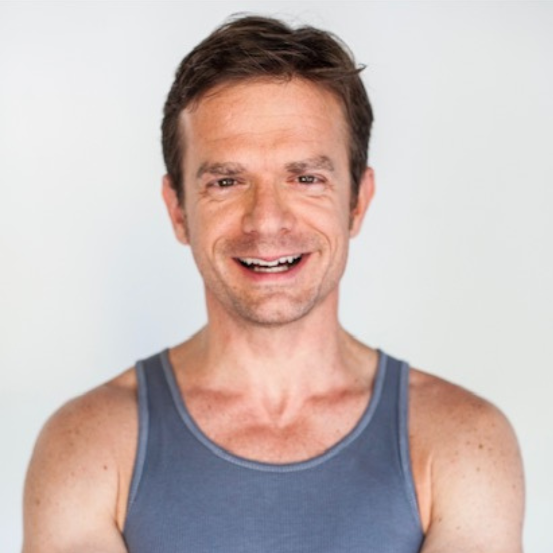 A man wearing a blue tank top smiles for the camera