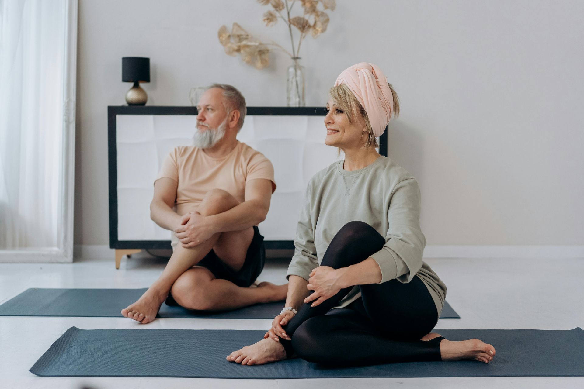 A man and a woman are sitting on yoga mats in a living room.