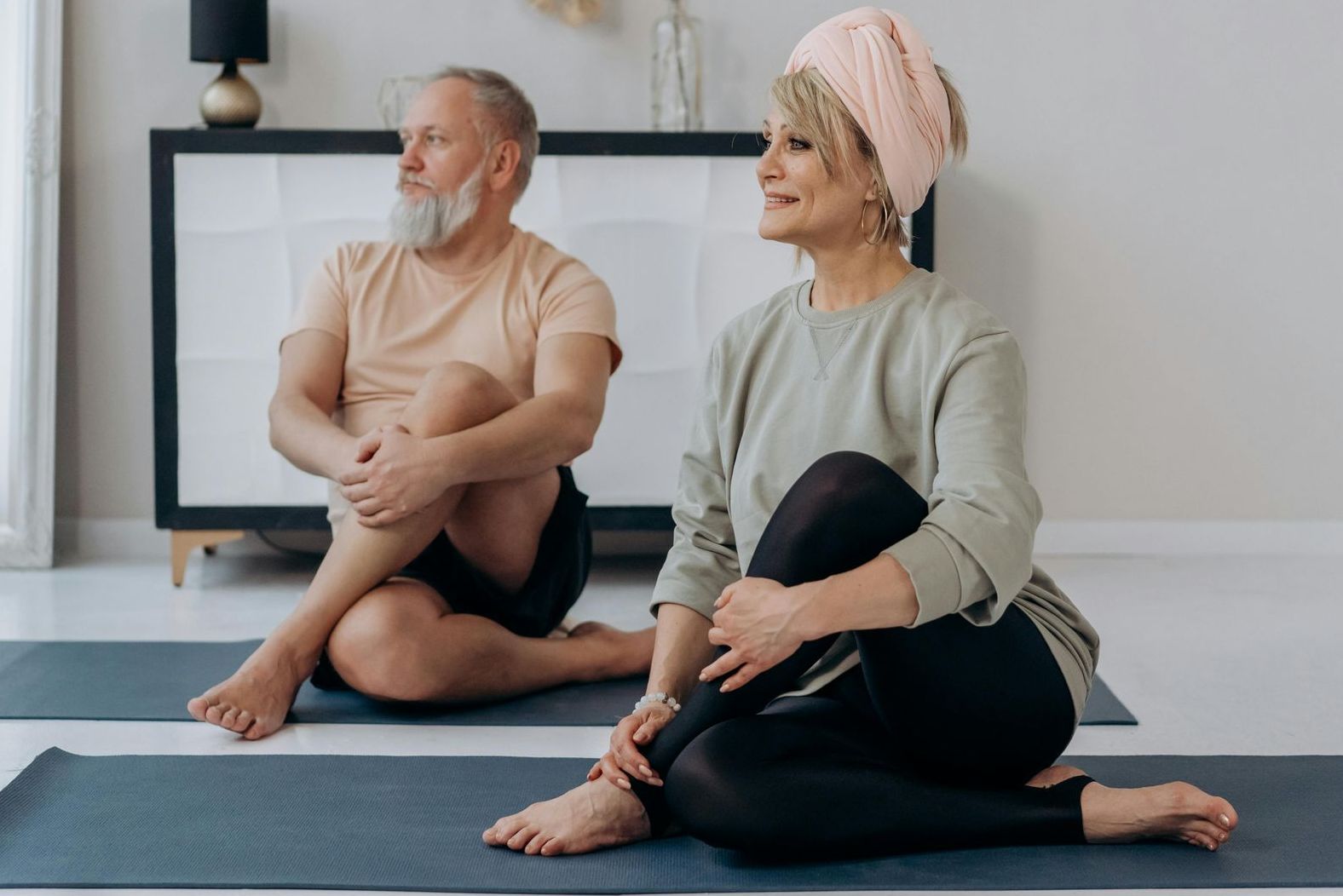 Senior couple doing seated yoga, smiling, in a light-filled room.