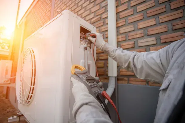 Un homme travaille sur un climatiseur à l'extérieur d'un bâtiment en briques.