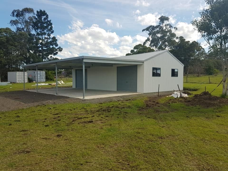 A White Metal Shed With a Carport, Set in a Grassy Rural Area Under a Partly Cloudy Sky — North Coast Sheds & Garages in Coraki, NSW