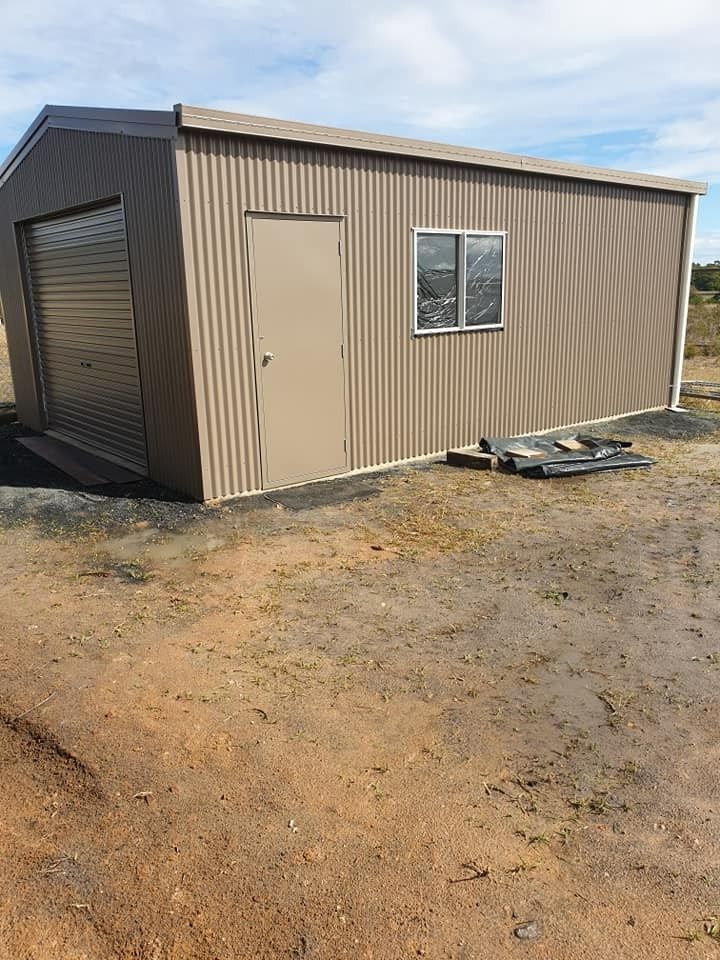 Tan Corrugated Metal Shed With a Garage Door, a Standard Door, and a Window; Set on a Dirt Surface  — North Coast Sheds & Garages in Coraki, NSW