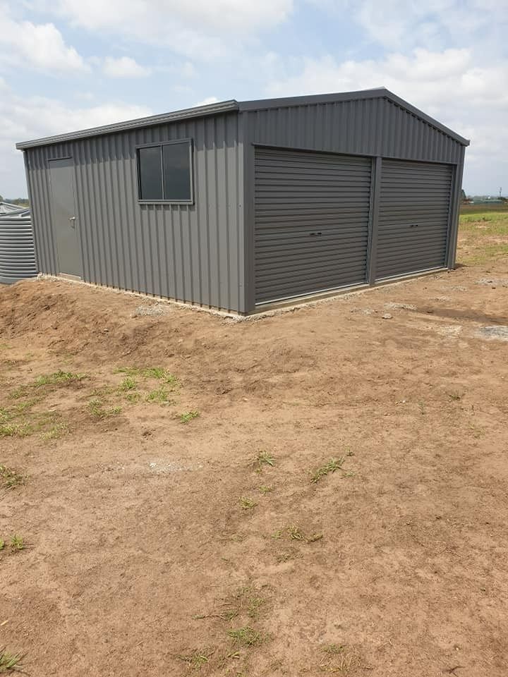 Gray Metal Shed With Two Garage Doors, a Side Door, and a Window, Set on a Dirt Lot Under a Cloudy Sky — North Coast Sheds & Garages in Coraki, NSW