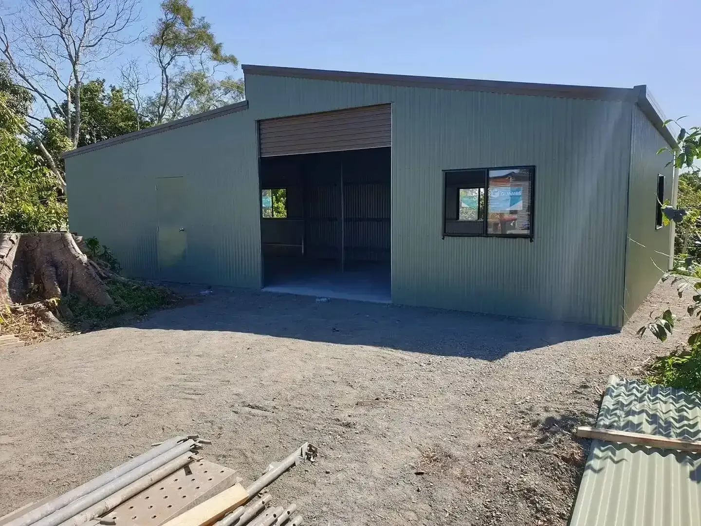Green Corrugated Metal Shed With an Open Garage Door and a Window. Gravel Driveway in Front of the Building — North Coast Sheds & Garages in Grafton, NSW