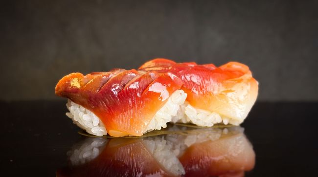 Nigiri sushi with glossy red fish on white rice, resting on a dark reflective surface