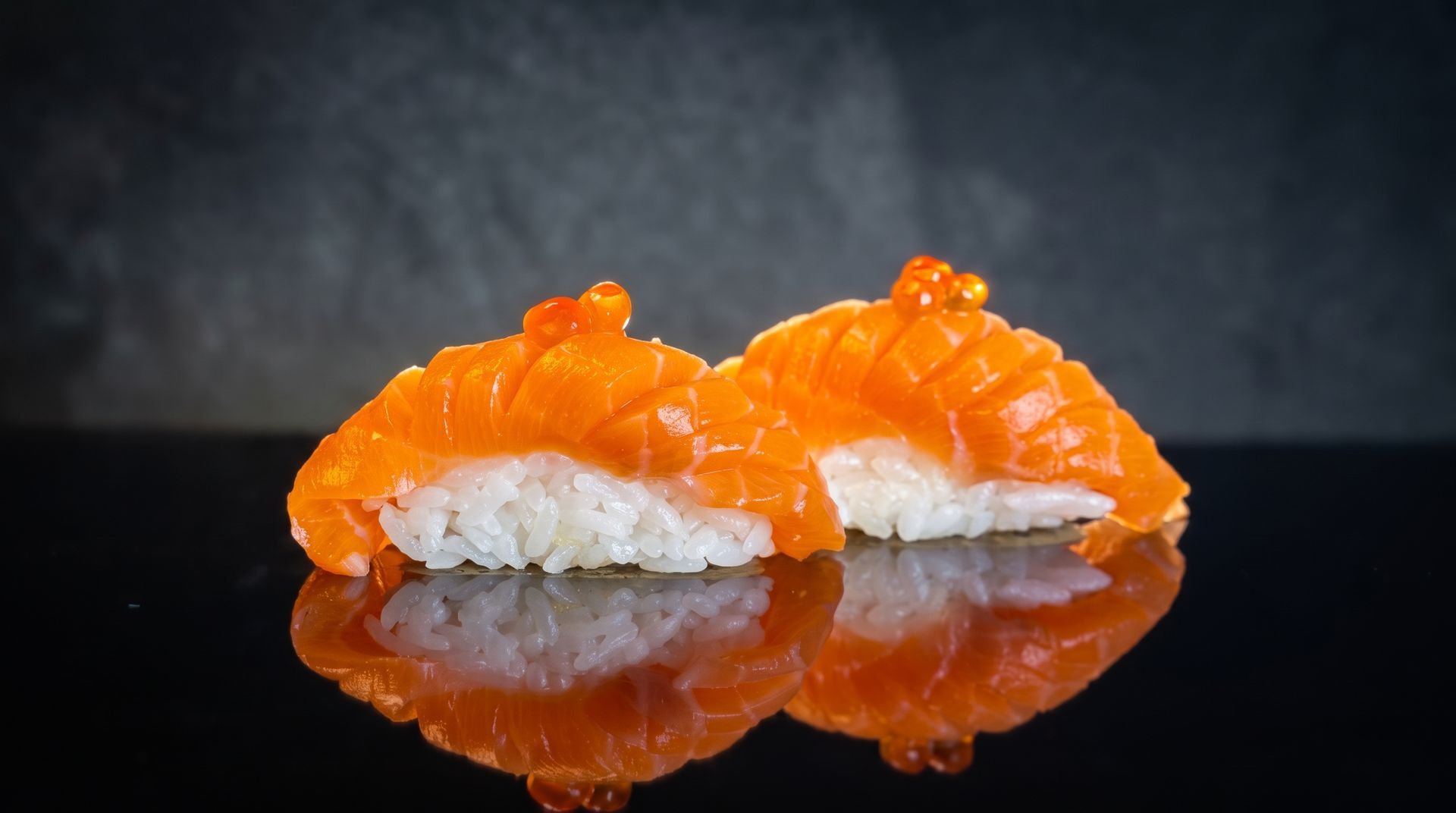 Two salmon nigiri sushi pieces on a glossy black surface, reflected below.