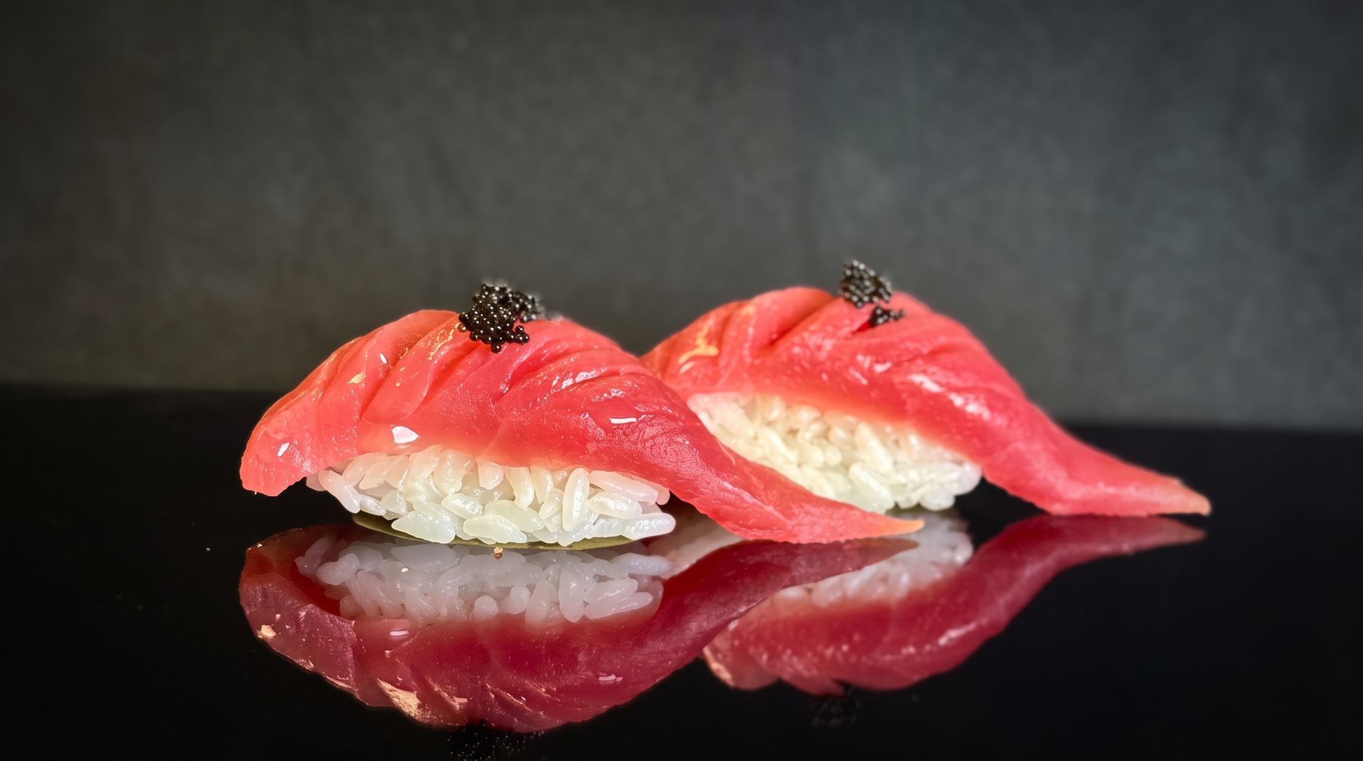 Two pieces of salmon nigiri sushi with black caviar on a glossy black surface