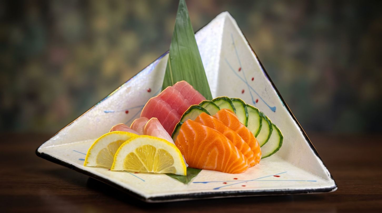 Assorted sashimi on a white plate with lemon wedges and cucumber garnish