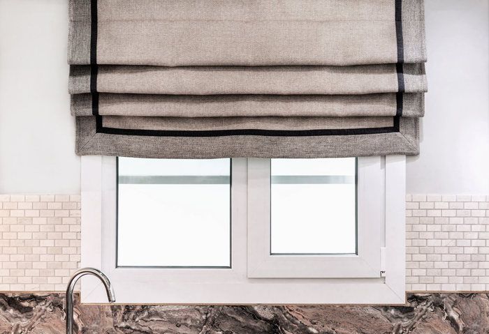 Close up of kitchen window over sink, with roman blind pulled up halfway over window.