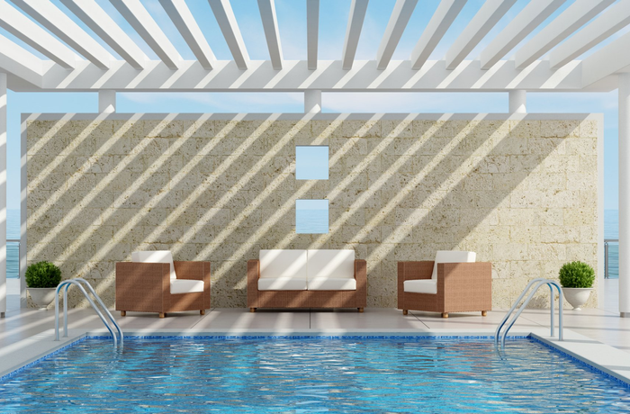 White metal fixed awning over pool with cane lounge suite in front of stone wall.