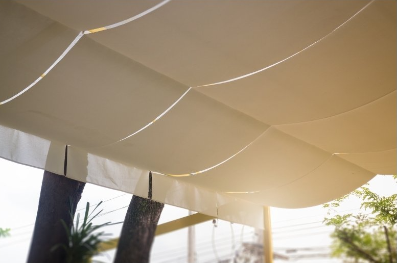 Flowing outdoor awning extended out with trees in background. and large potted plants on balcony in the background.