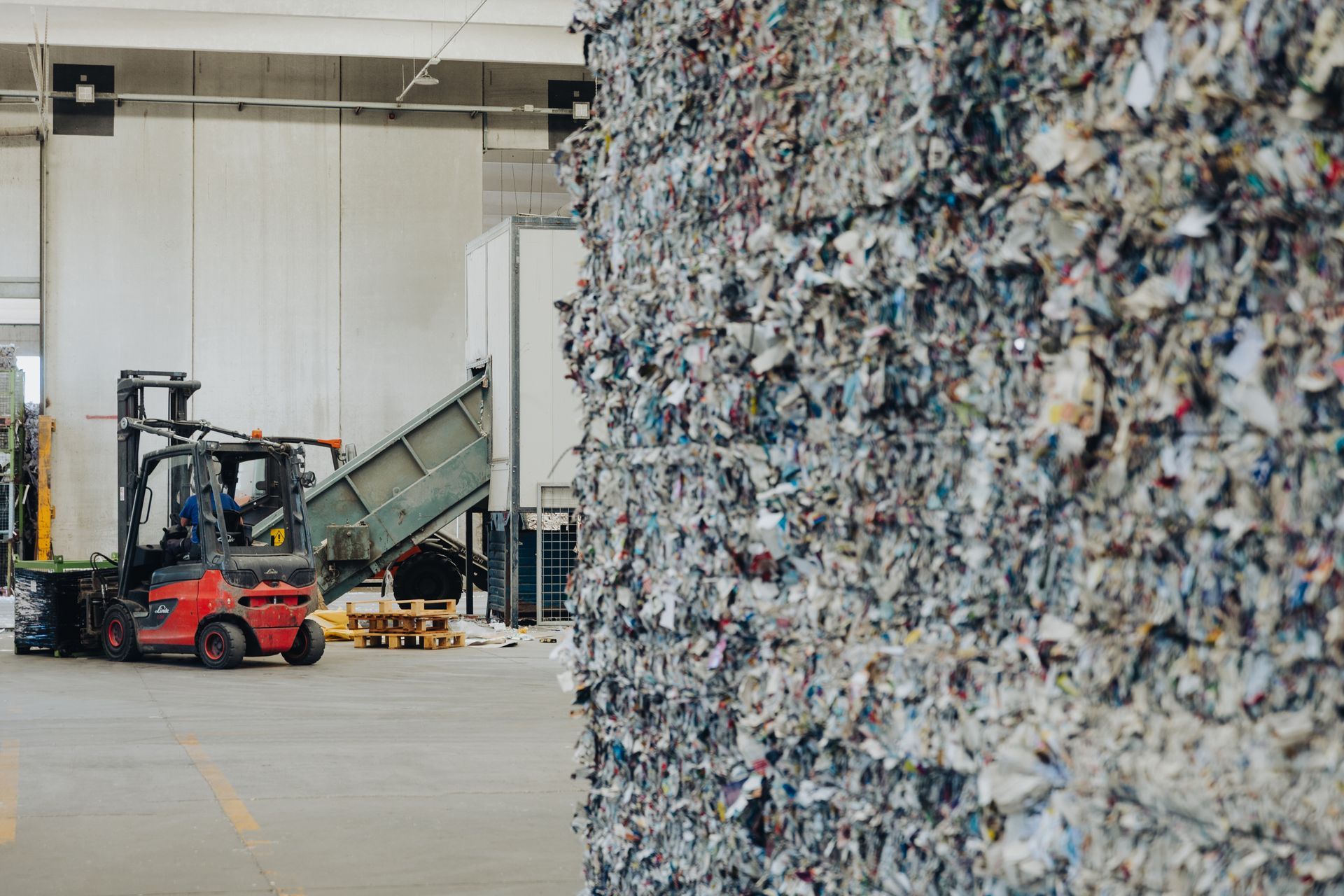 Carrello elevatore in un impianto di riciclaggio accanto a un'enorme parete di rifiuti di carta e plastica compressi.