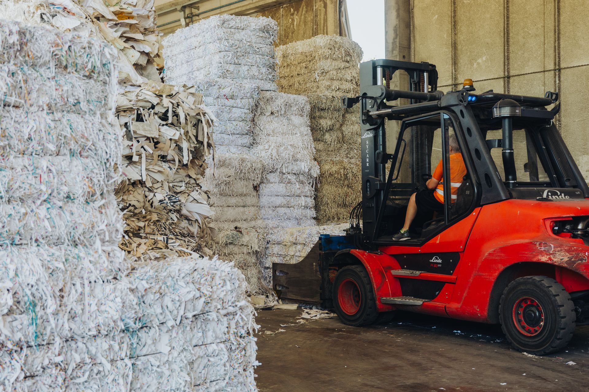 Carrello elevatore rosso in un magazzino che sposta balle impilate di pellicola di plastica riciclabile