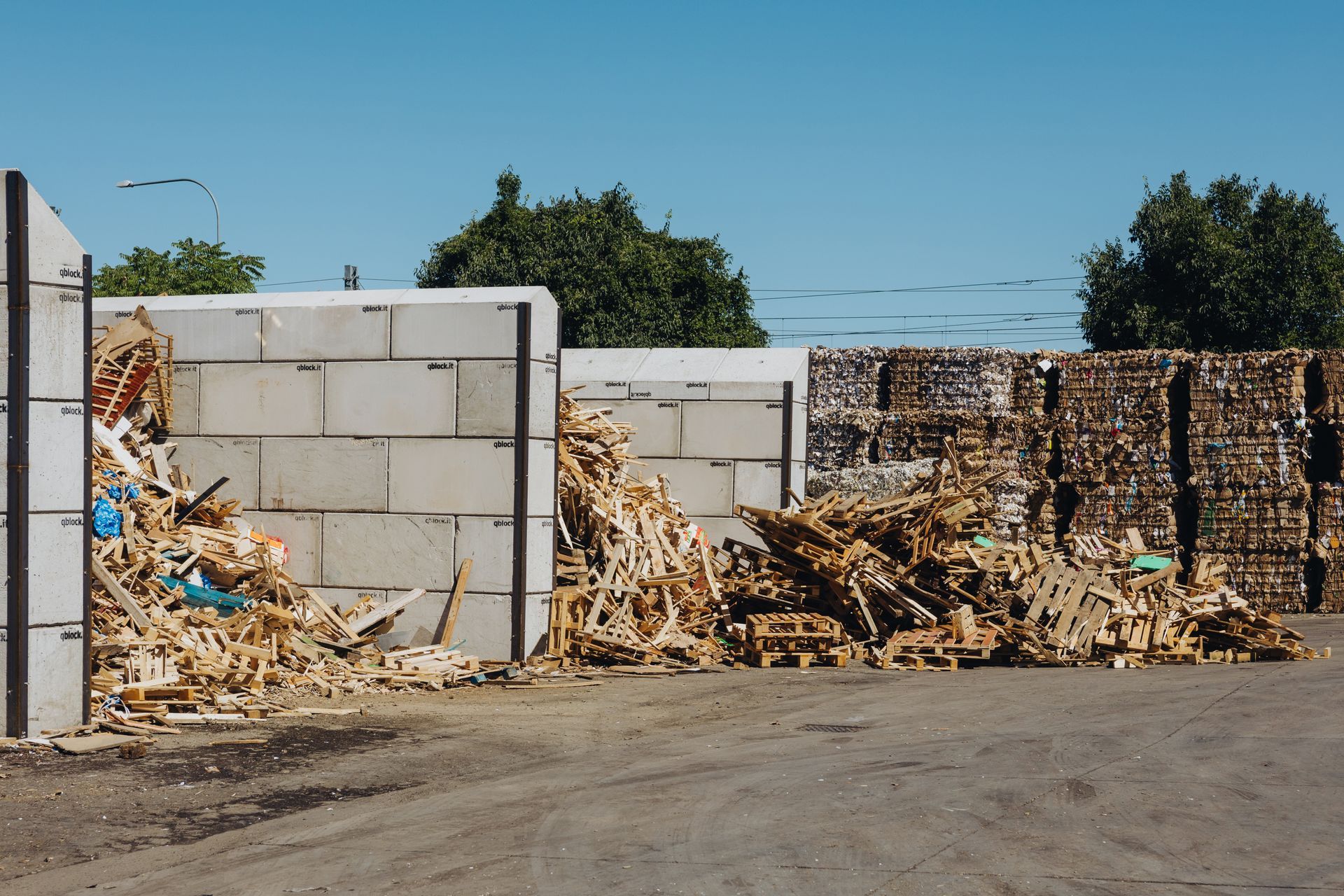 Cumuli di legno e detriti accanto a un muro di blocchi di cemento in un'area industriale all'aperto.