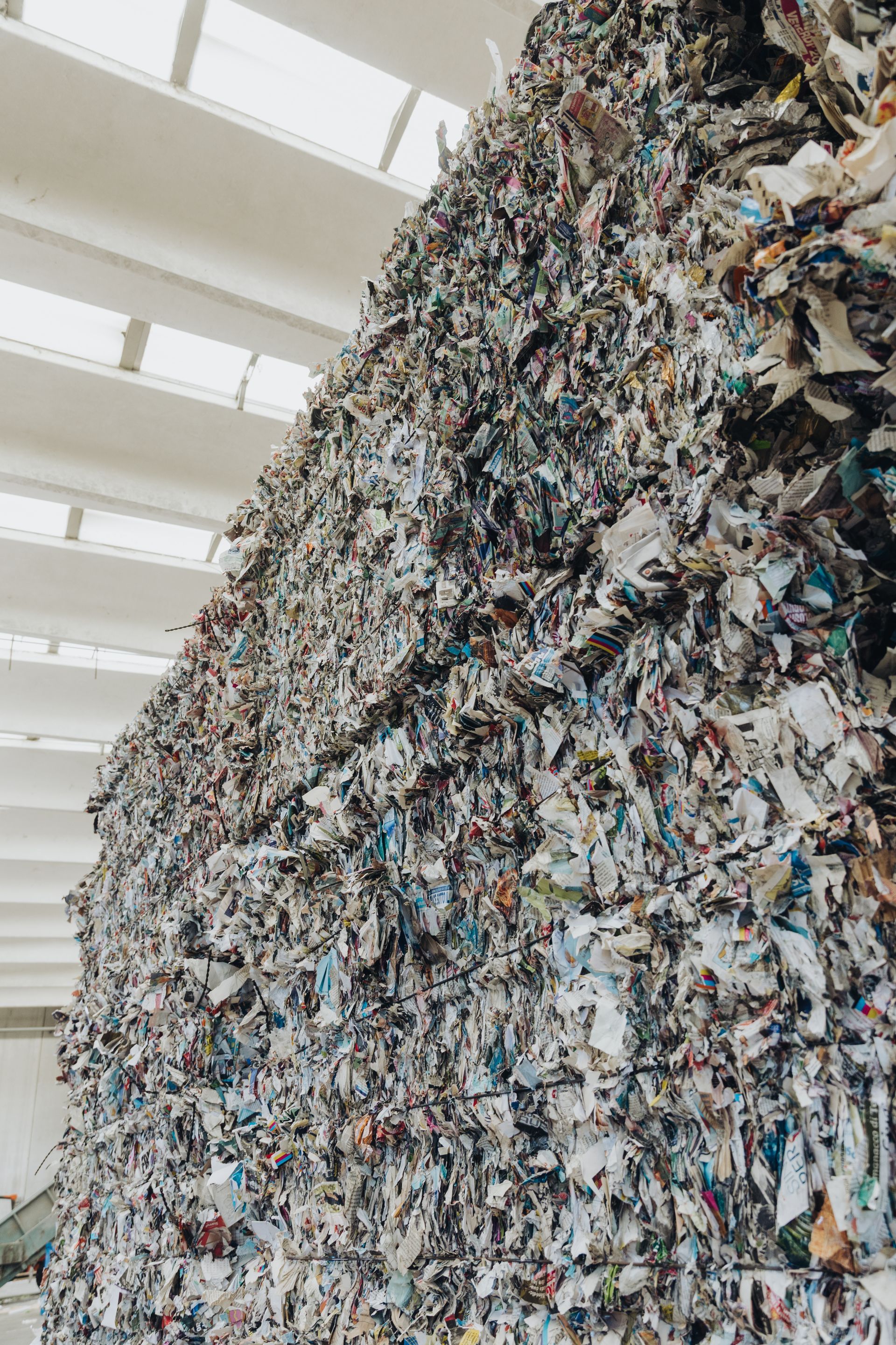 Un'enorme pila di carta tritata e scarti di plastica all'interno di un luminoso magazzino industriale.