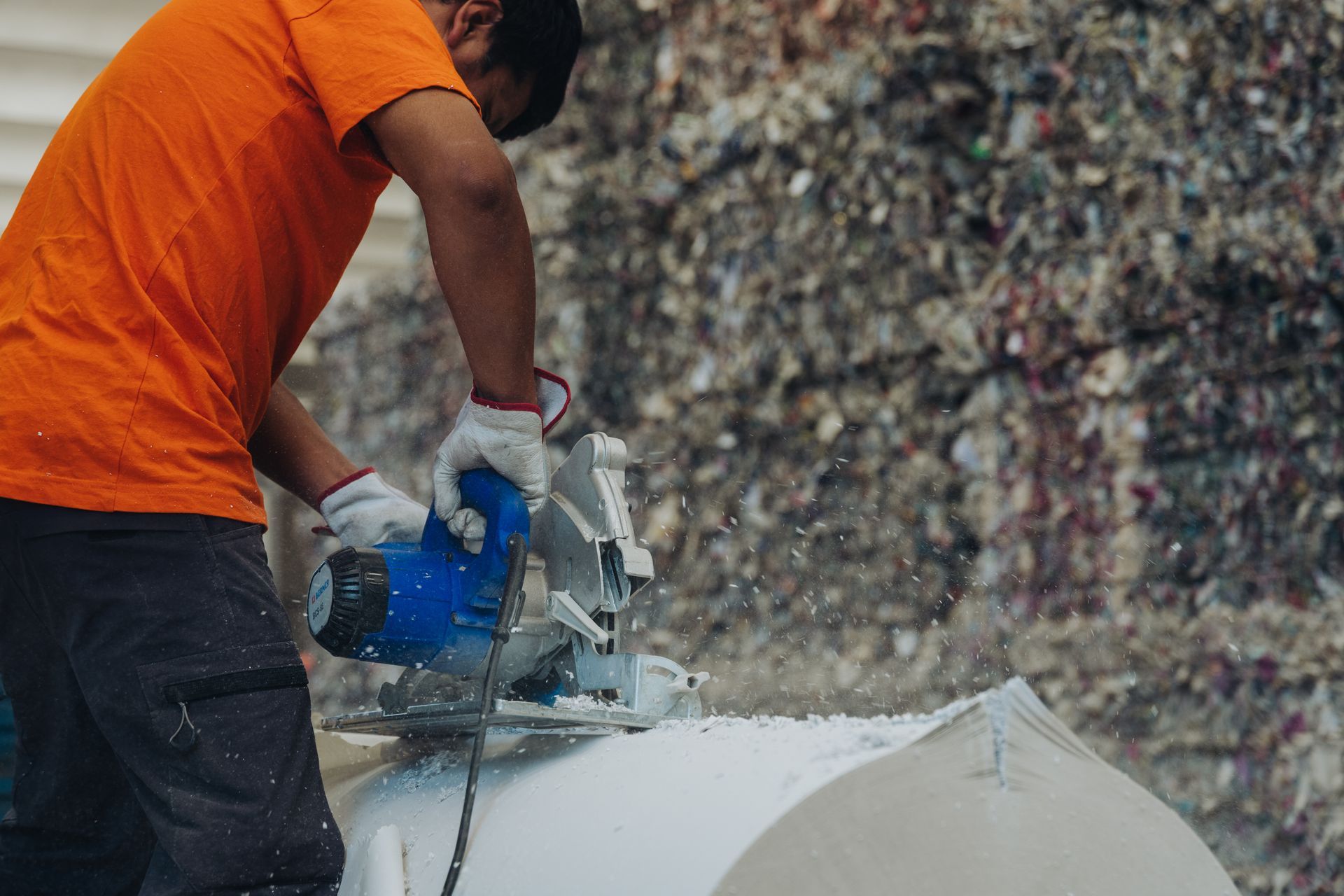 Un operaio con una maglietta arancione taglia una tavola con una sega circolare in un cantiere.