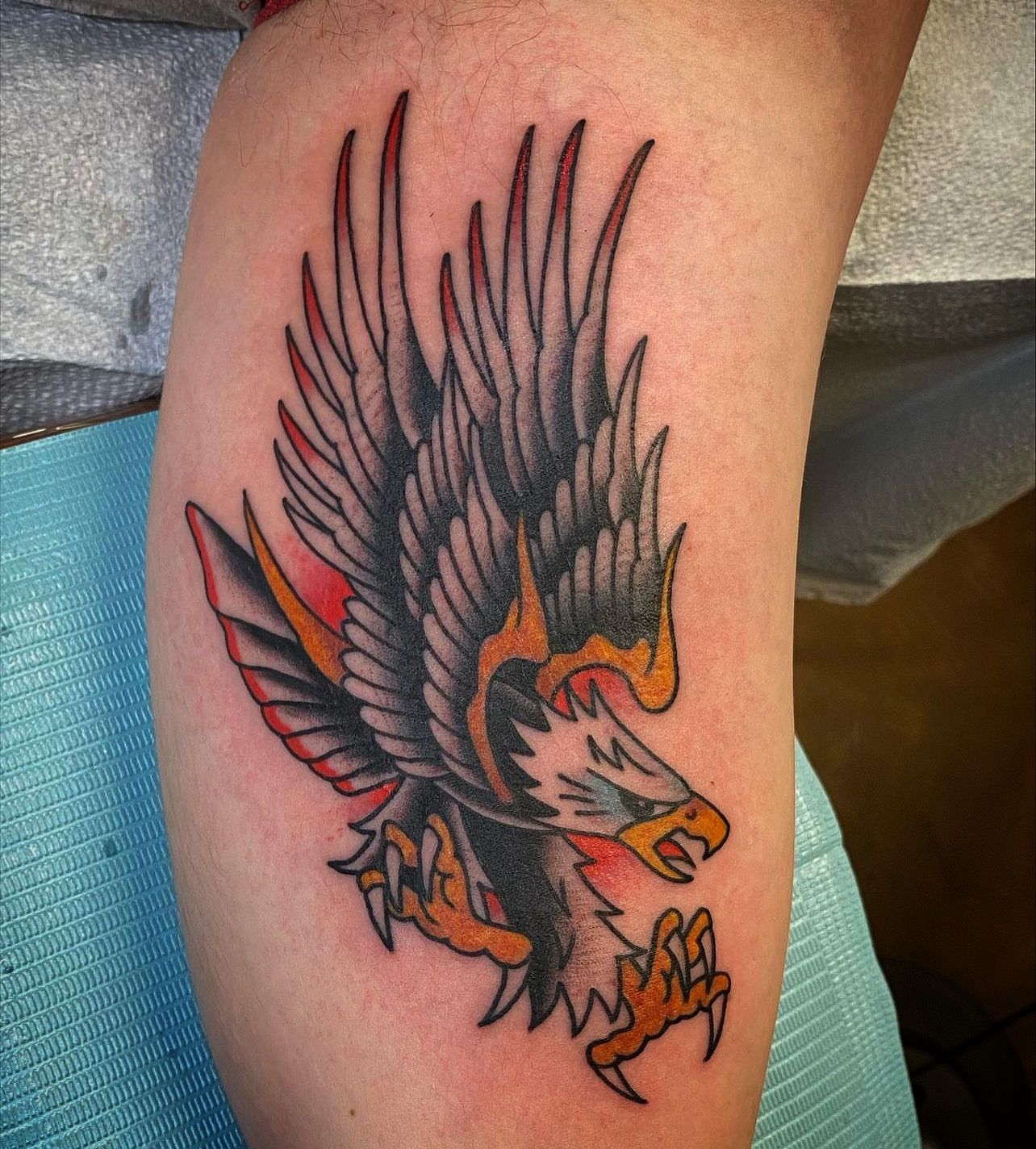 Tattoo of an eagle in flight with red, black, and orange details, on a person's arm.