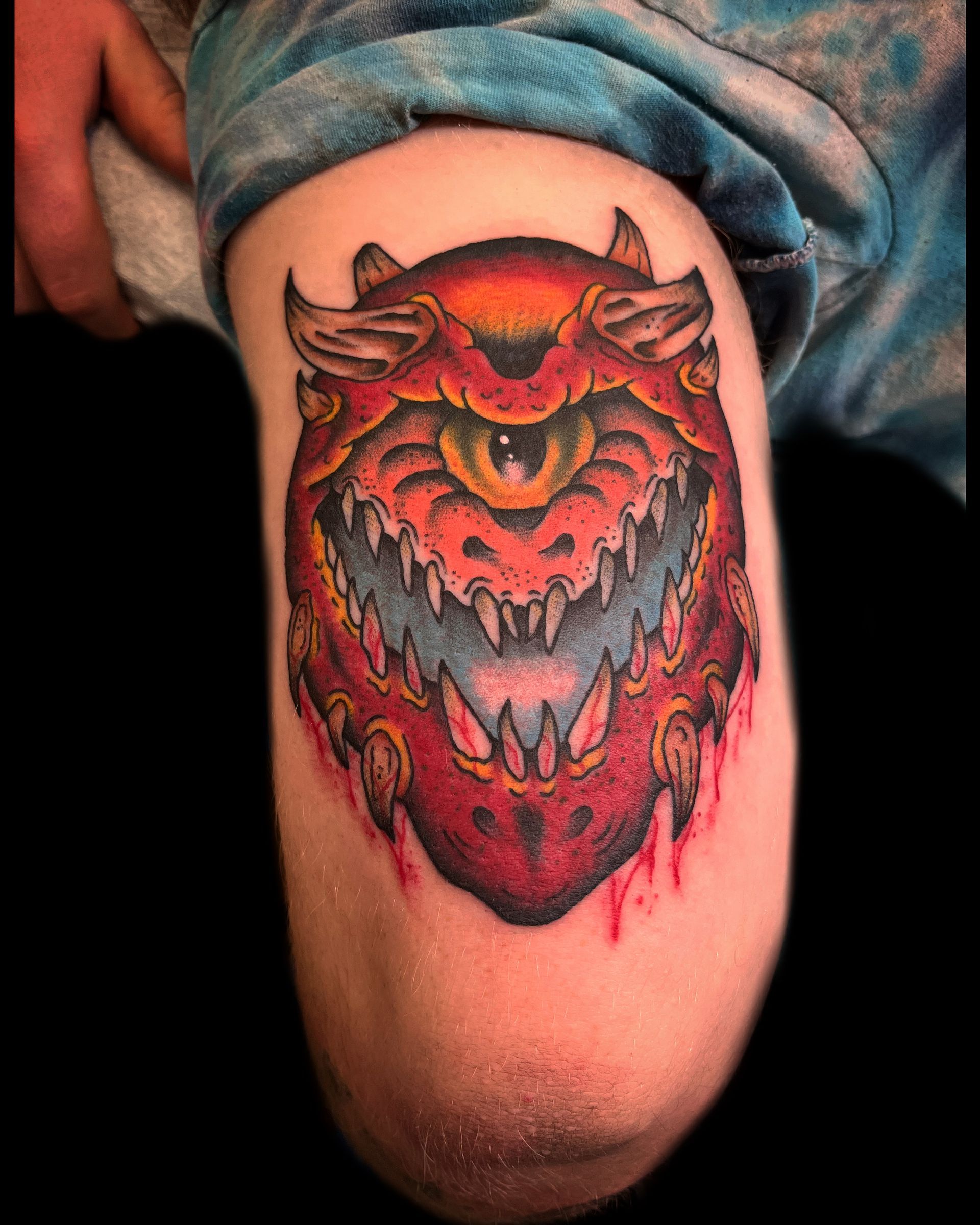 Tattoo of a red, one-eyed, demonic creature on a person's upper arm.