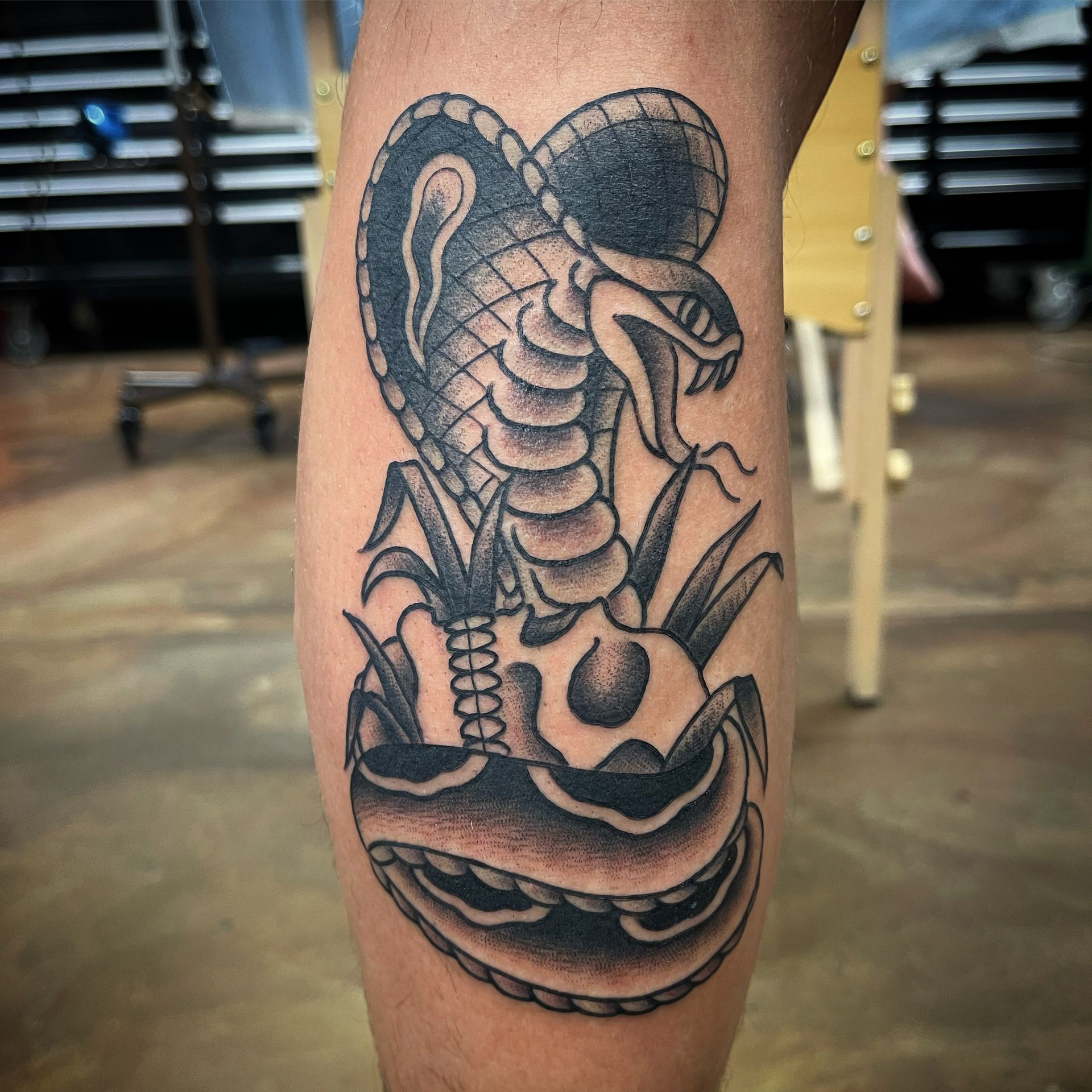 Black and gray cobra tattoo on leg, with skull and leaves.