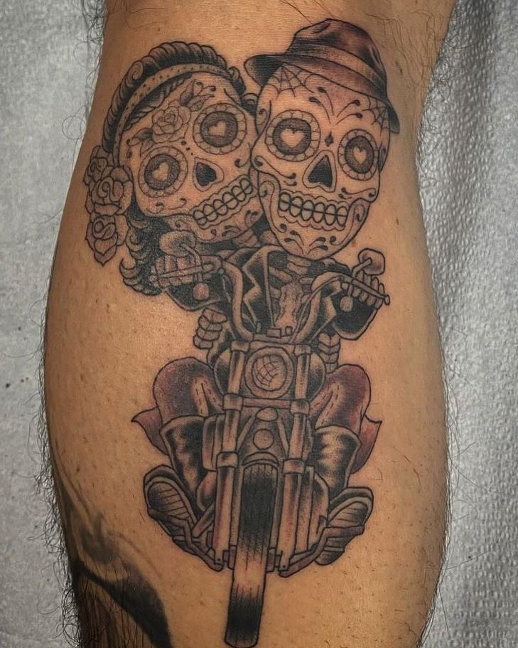 Tattoo of sugar skull couple on a motorcycle. They have heart eyes.