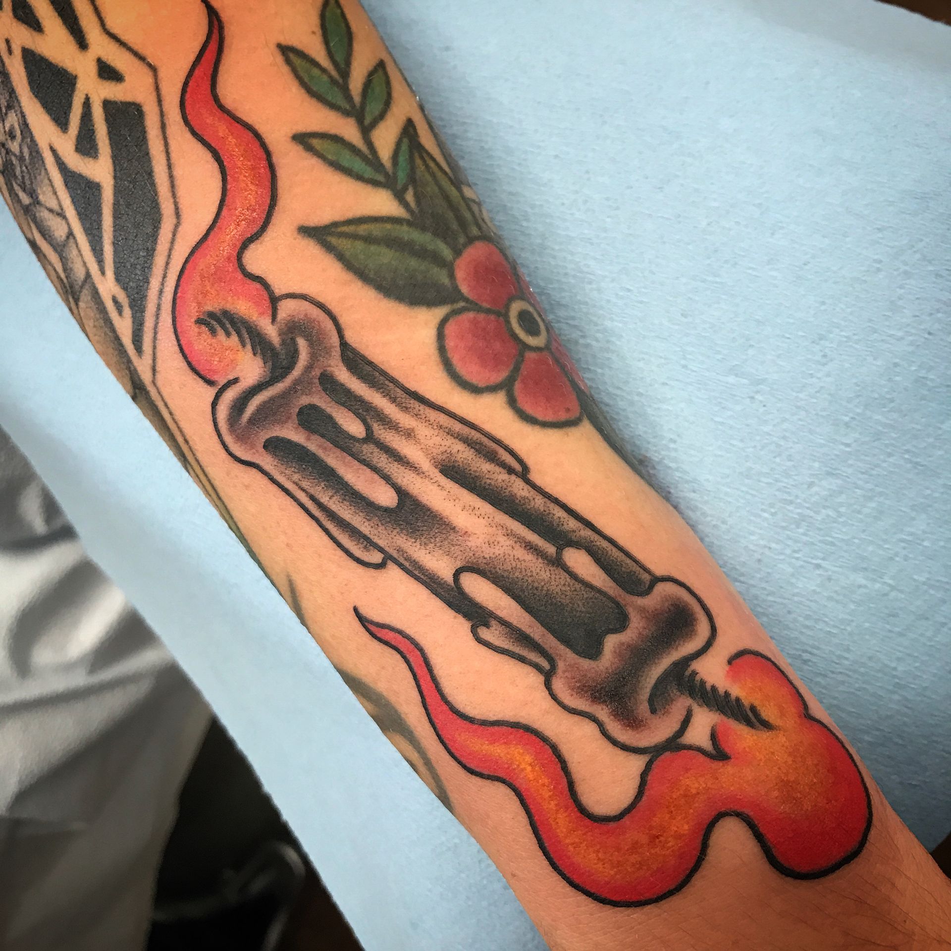 Tattoo of a candle, burning with orange flames, on a person's arm. Also, floral tattoos.
