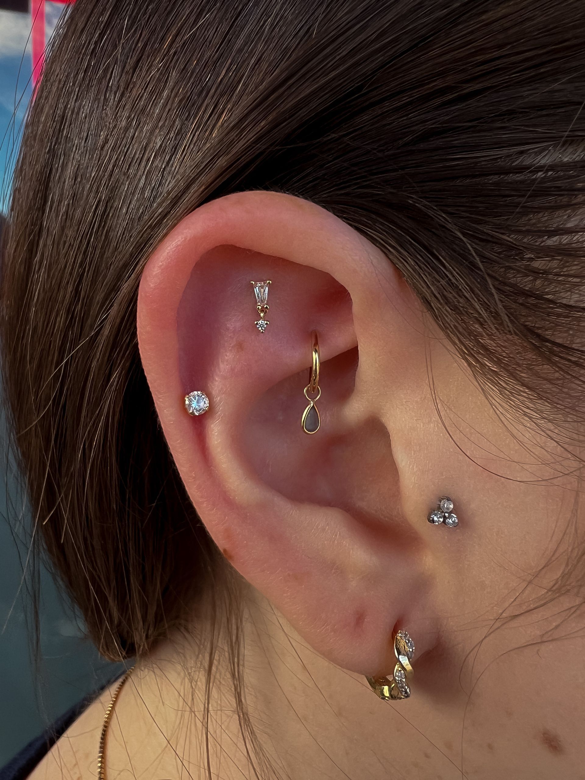Ear with multiple piercings and gold and silver jewelry, including studs and a dangling hoop.