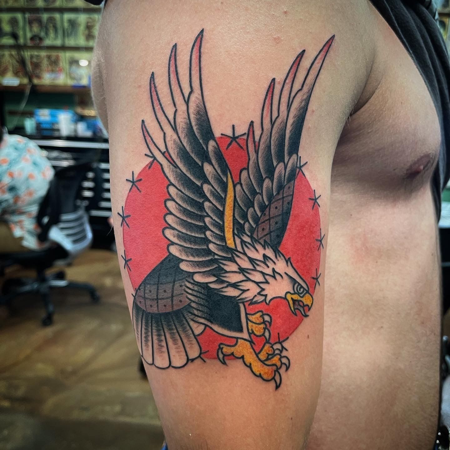 Tattoo of a black eagle with outstretched wings and yellow talons, over a red circle with a star border.