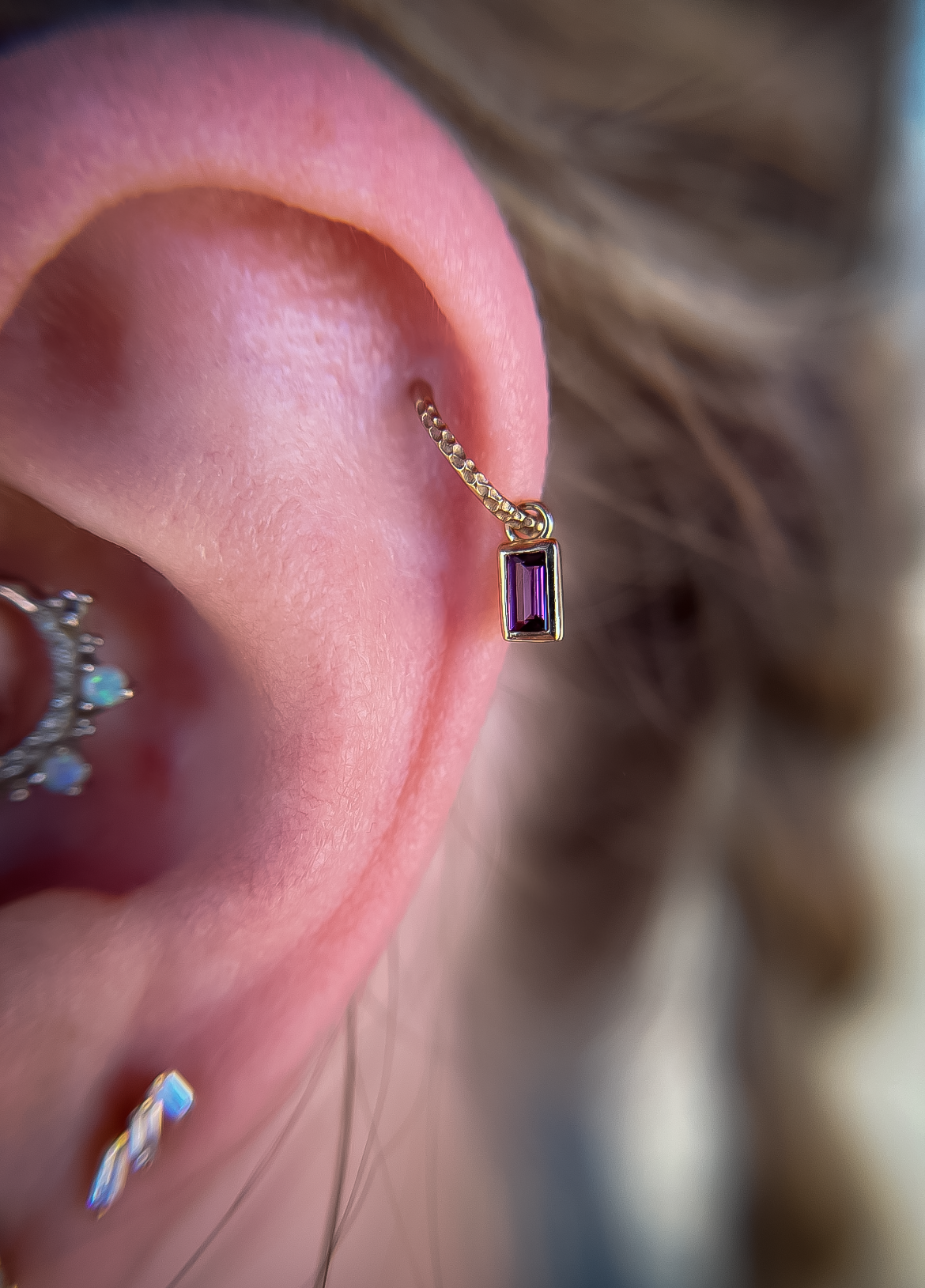 Close-up of an ear with a gold hoop and purple rectangular earring gauge