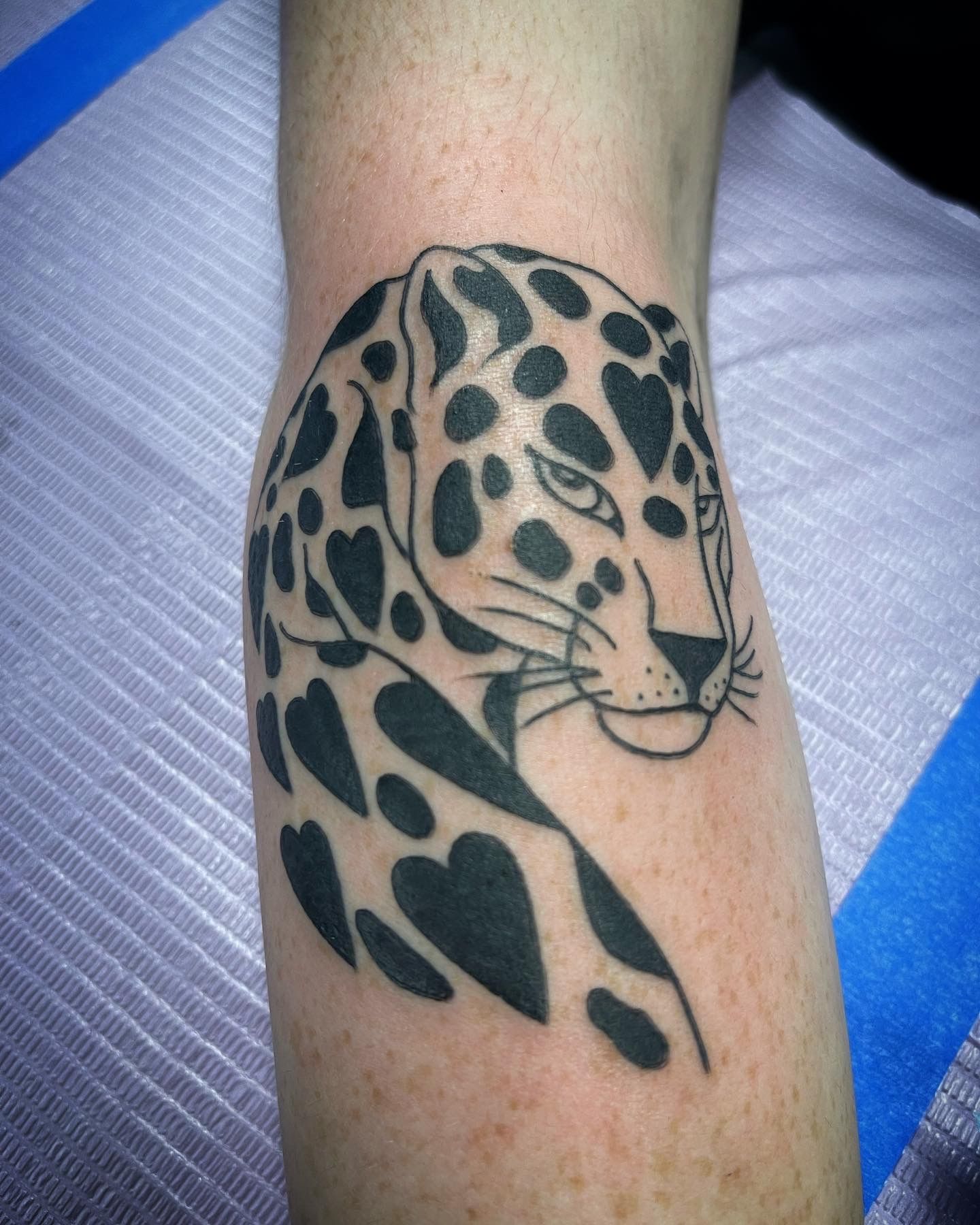 Black and white tattoo of a leopard on a leg. The spots are heart-shaped.