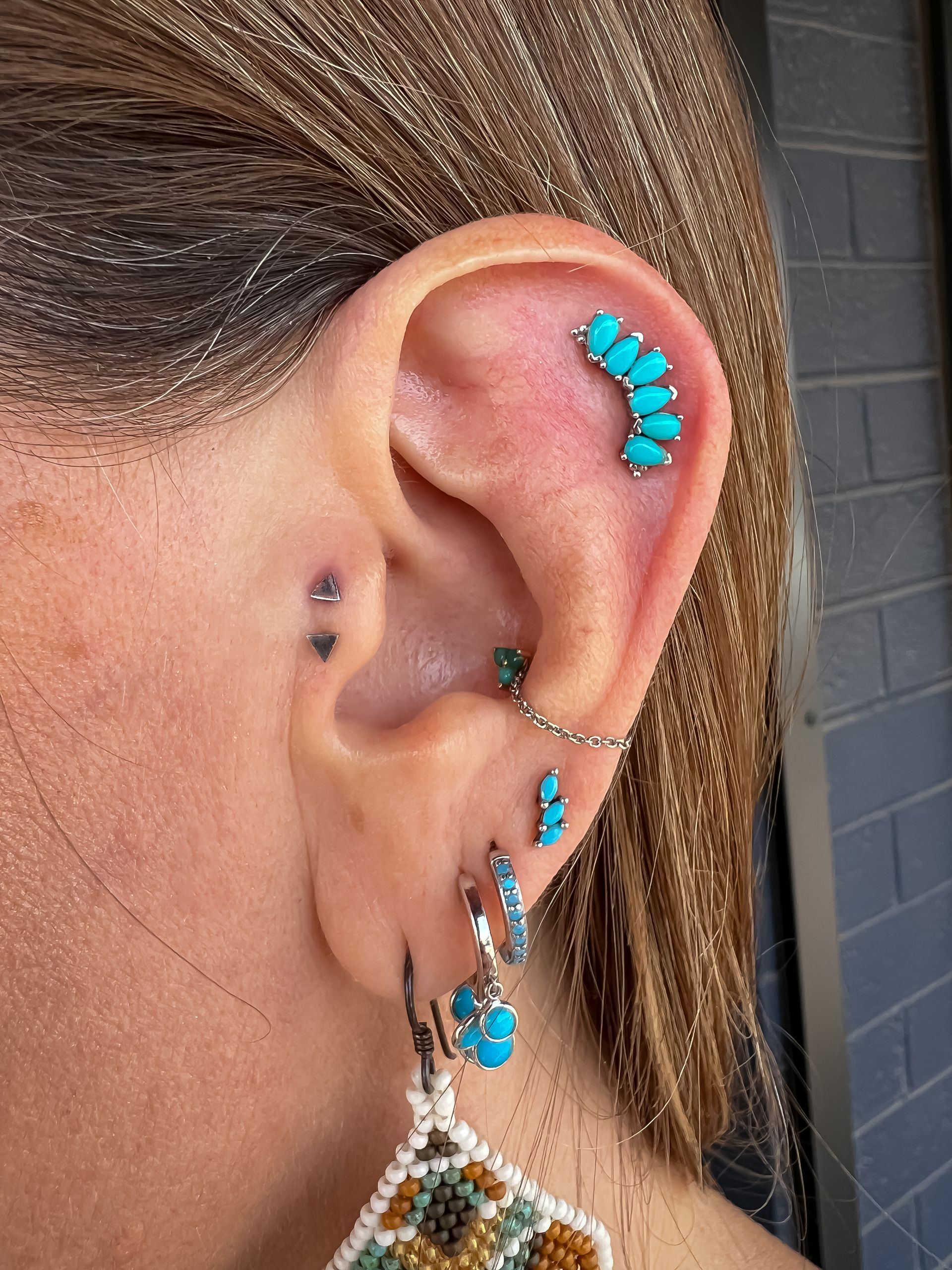 Close-up of an ear with turquoise and silver earrings and multiple turquoise ear piercings.
